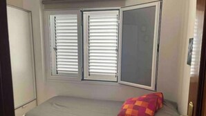A small bedroom with a single bed, a window with blinds, and a door. - Casa Típica Canaria (Playa Honda)