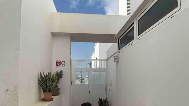 A narrow outdoor corridor with a white door, potted plants, and a small white gate. - Casa Típica Canaria (Playa Honda)