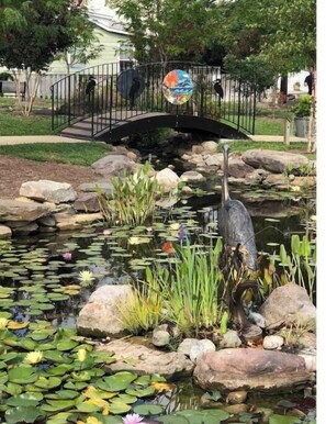 Stroll across the serene garden pond, featuring a picturesque bridge and a lifelike heron sculpture.