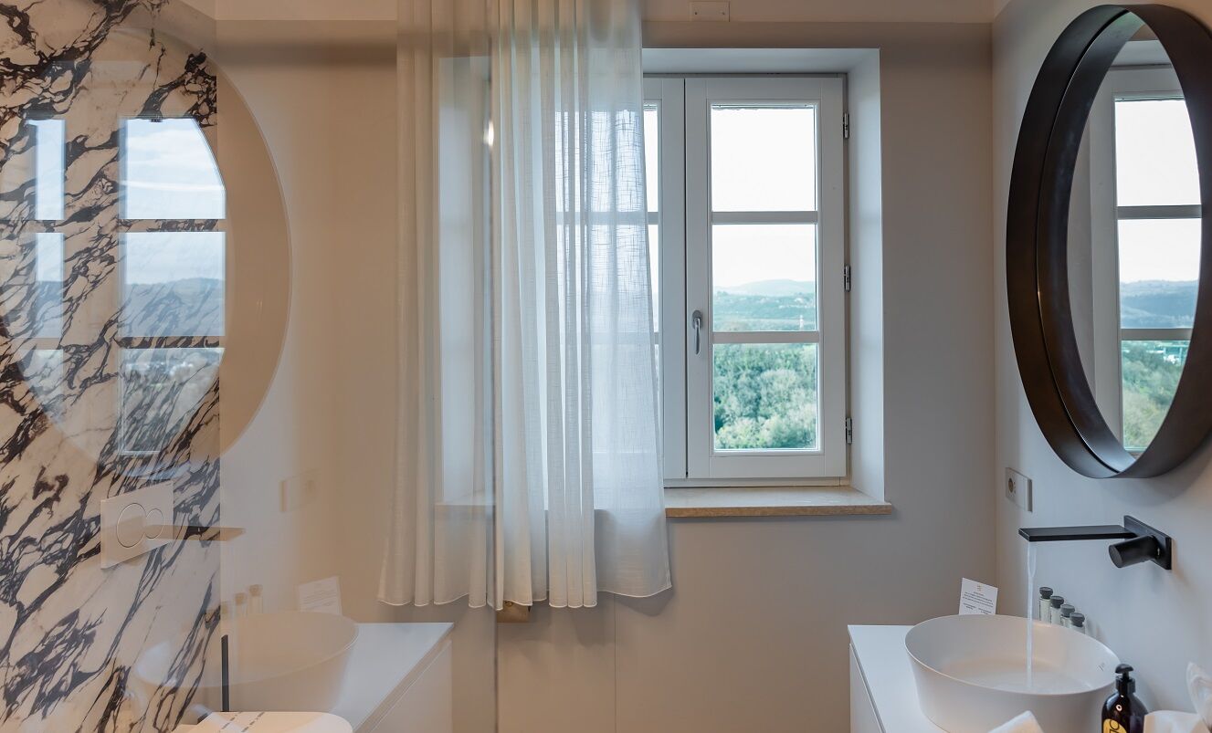 Une salle de bain avec un mur en marbre, une fenêtre donnant sur un beau paysage, un lavabo et un miroir.