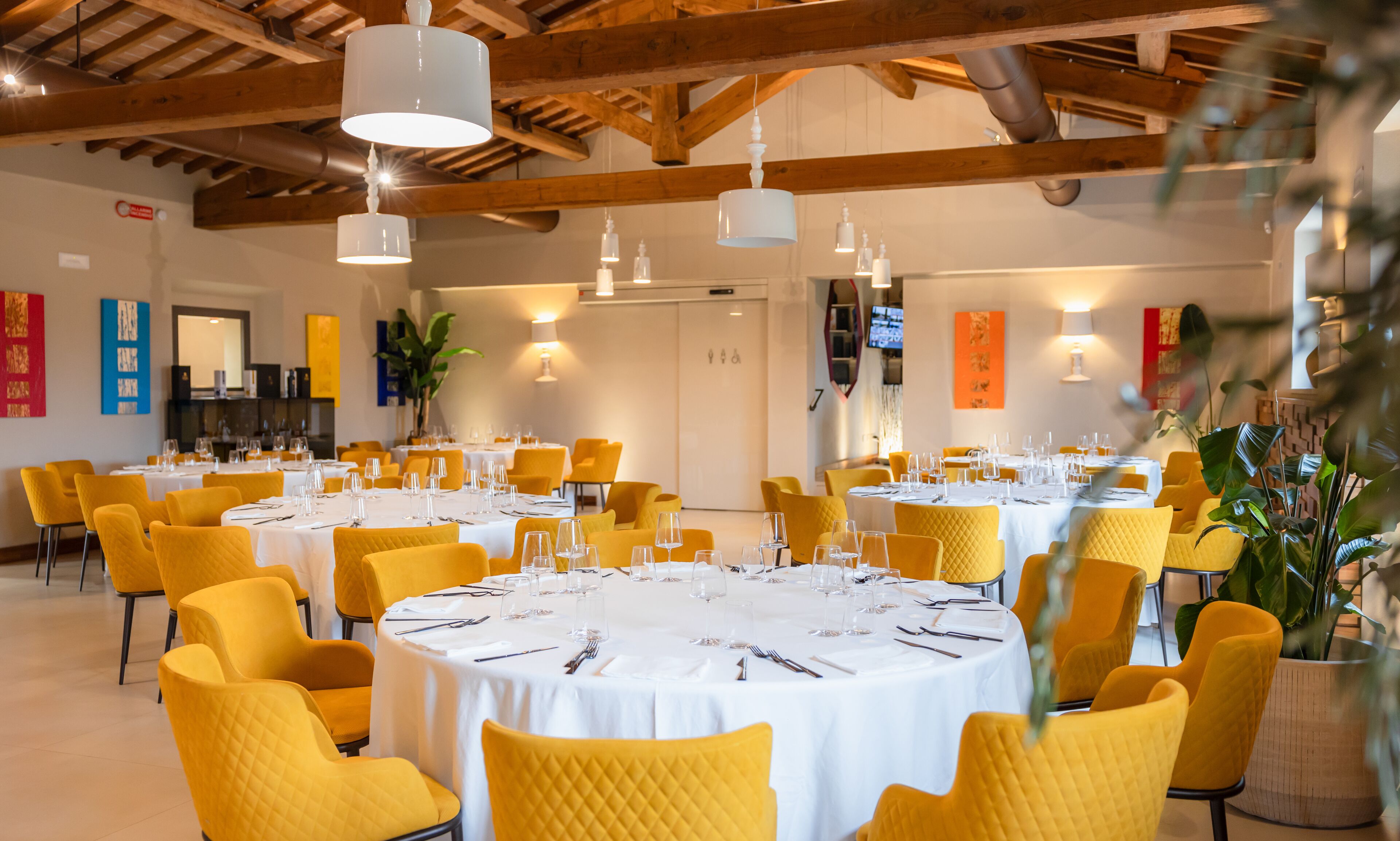A dining area with round tables, yellow chairs, white tablecloths, and pendant lighting.