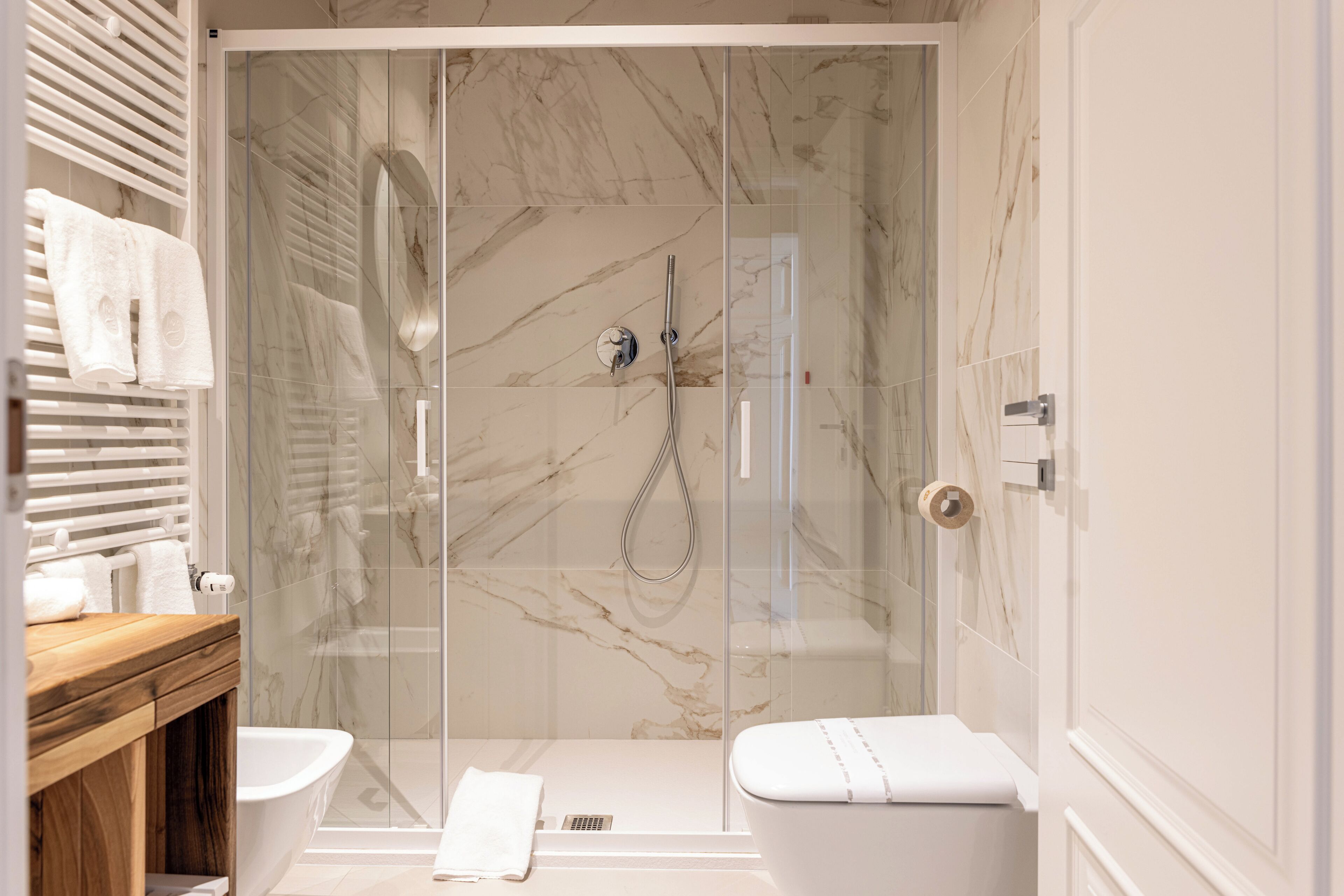 Un baño moderno con ducha envuelta en vidrio, tocador de madera y un inodoro blanco.