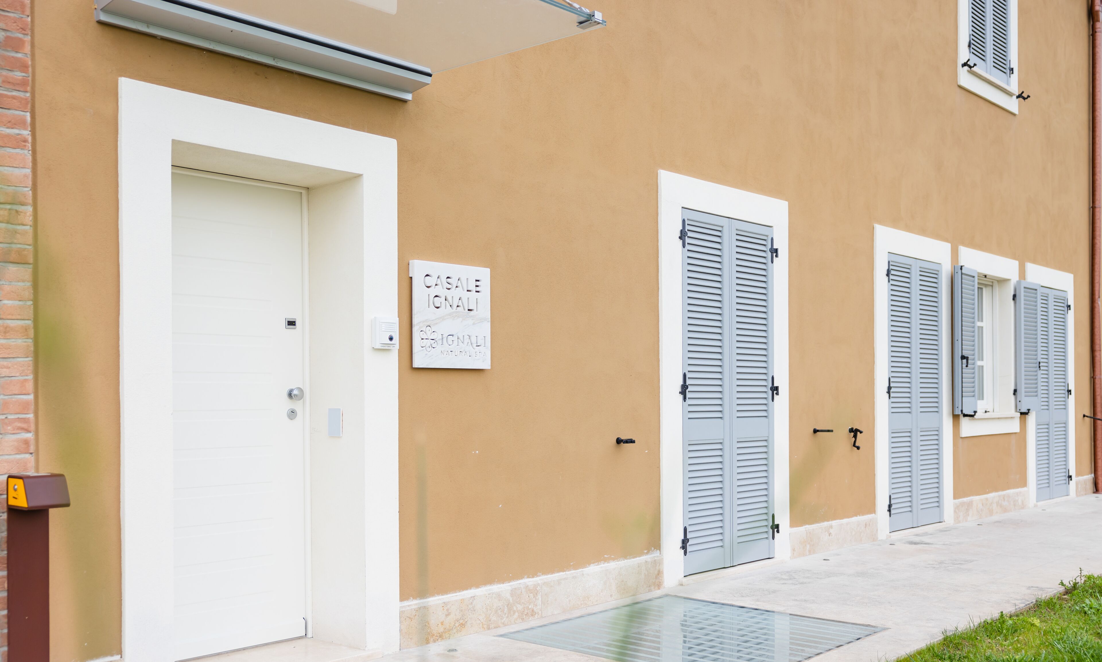 A building with a beige exterior, white doors, and shutters. A sign on the wall reads "CASALE SIGNALI NATURAL SPA".