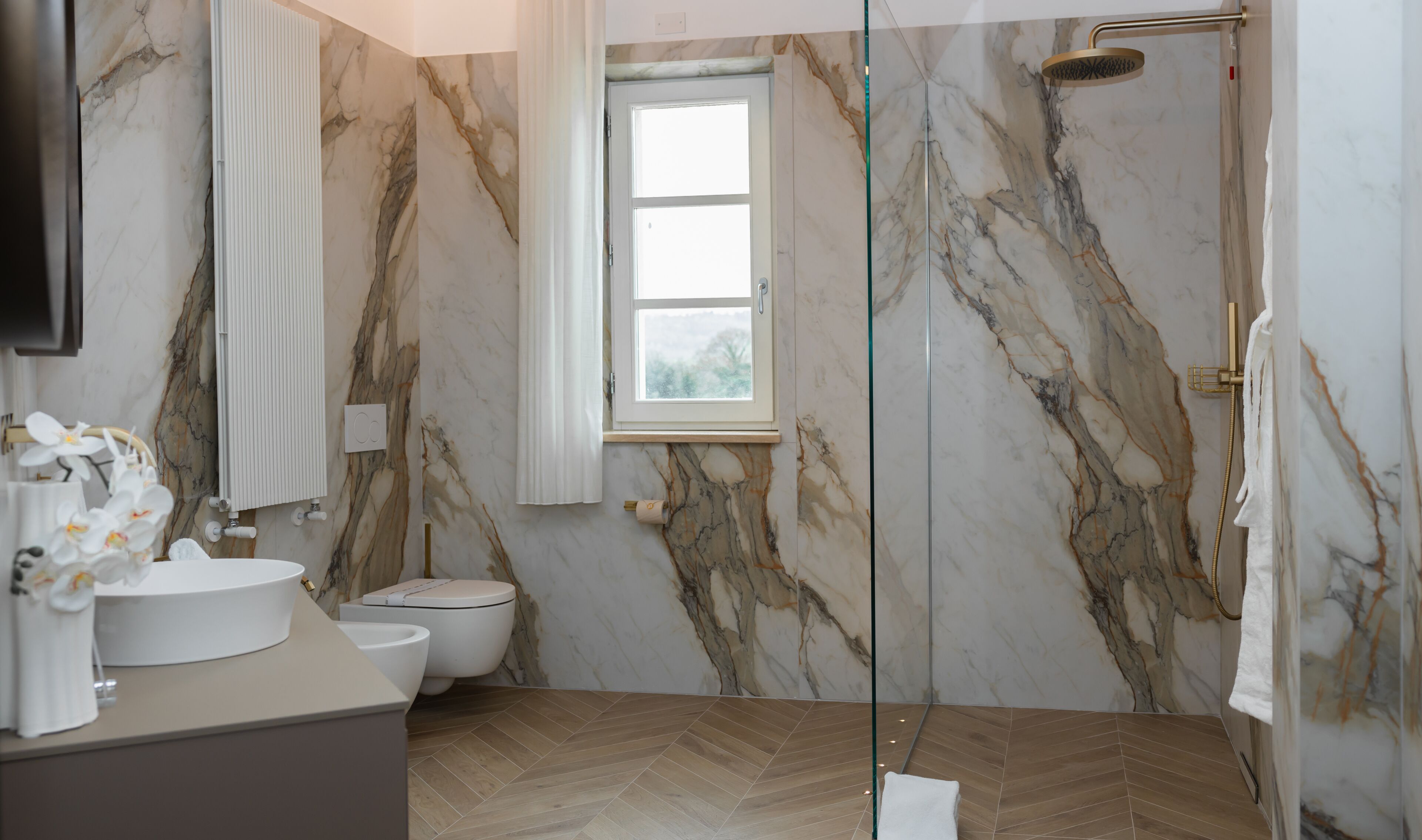 Un baño con paredes de mármol, un inodoro, un lavamanos, una ducha y una ventana.