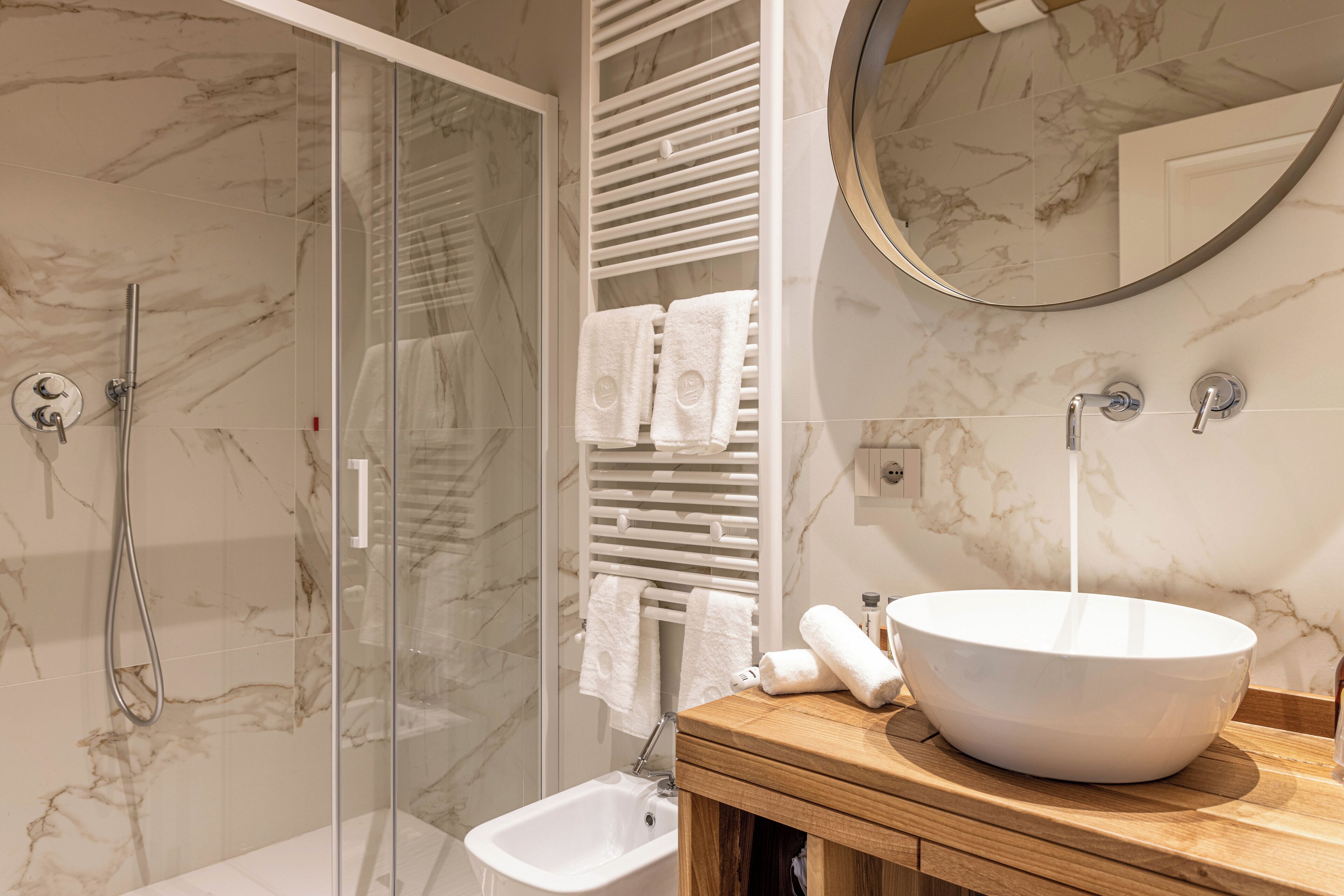 A modern bathroom with a glass shower enclosure, a white sink with a marble countertop, and a towel rack with white towels.