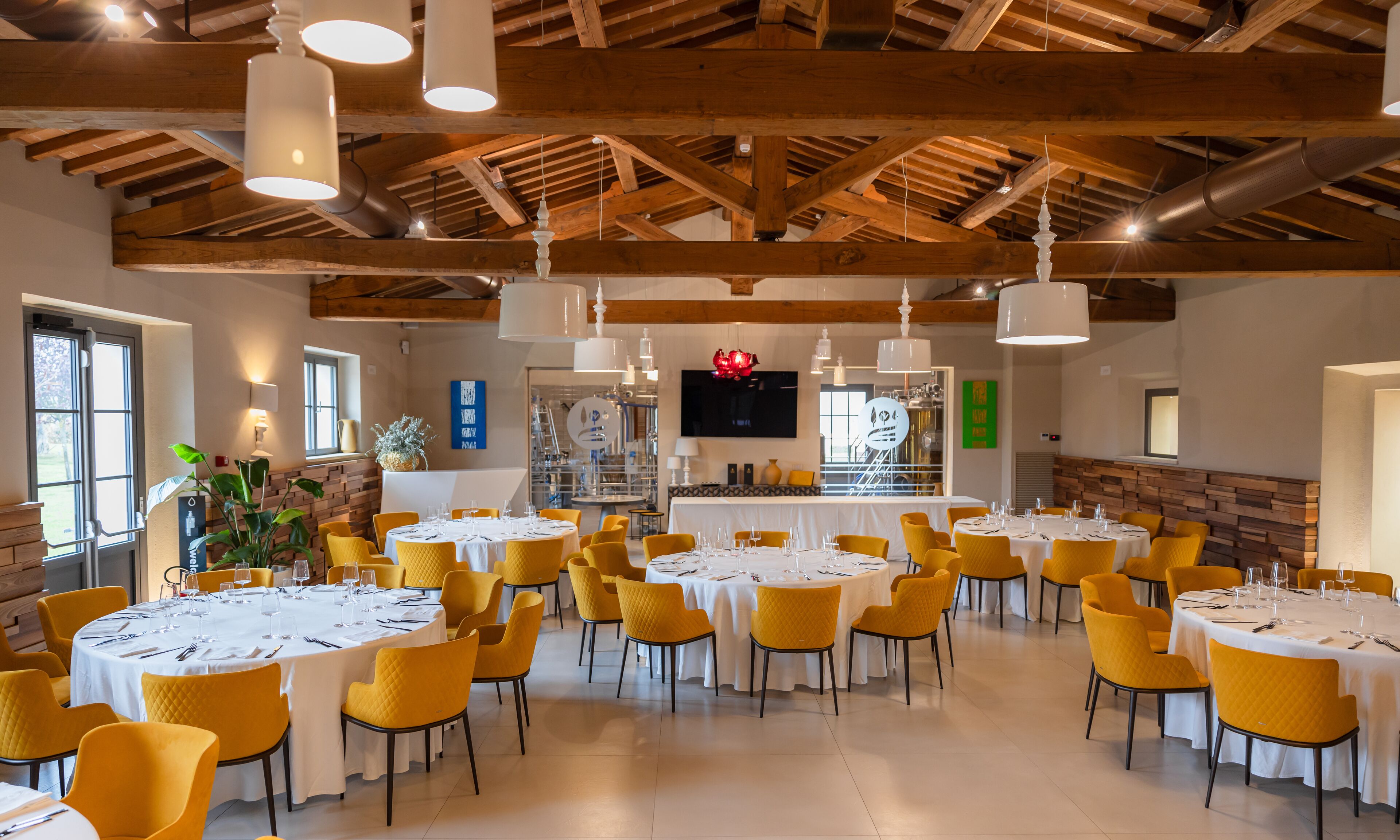 A spacious dining area with multiple round tables, yellow chairs, and a wooden ceiling.