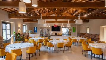 A spacious dining area with multiple round tables, yellow chairs, and a wooden ceiling.