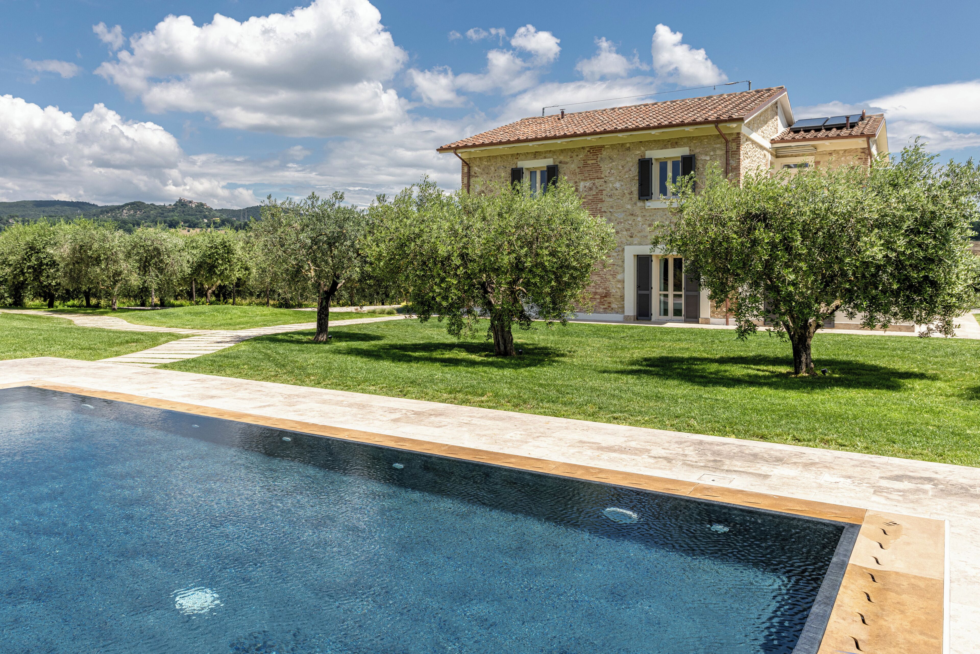 A poolside view of a house with a tiled roof, surrounded by a well-maintained lawn and trees.