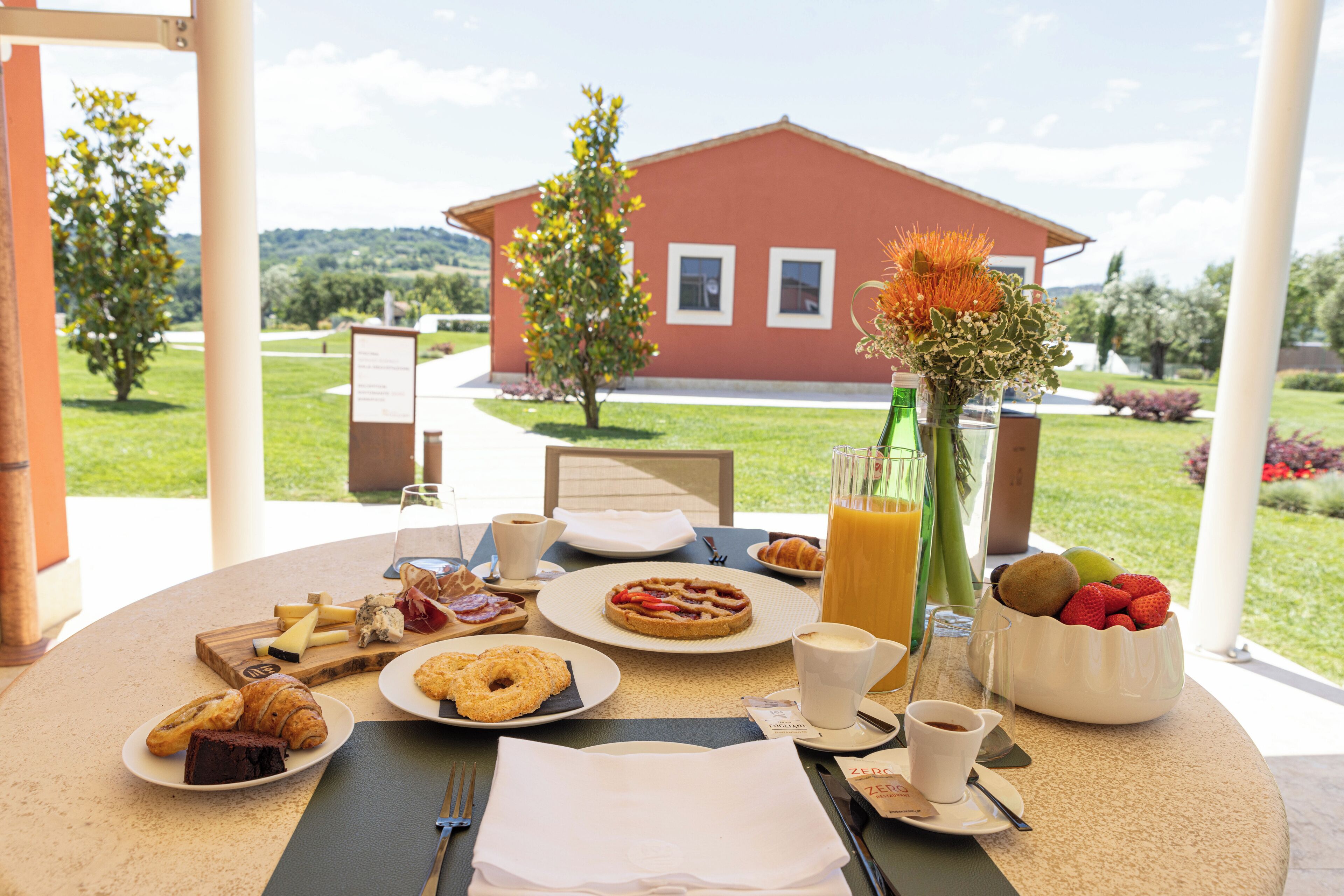 Una mesa de desayuno con croissants, pasteles, fruta, café y jugo.