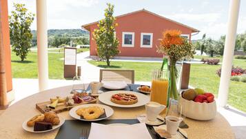 Mesa de café da manhã com croissants, doces, frutas, café e suco.