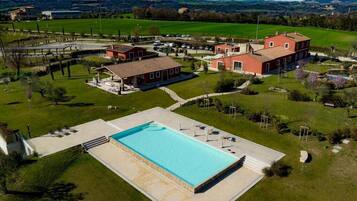 Vista aérea de una propiedad con piscina, un edificio grande de color rojo y campos verdes circundantes.