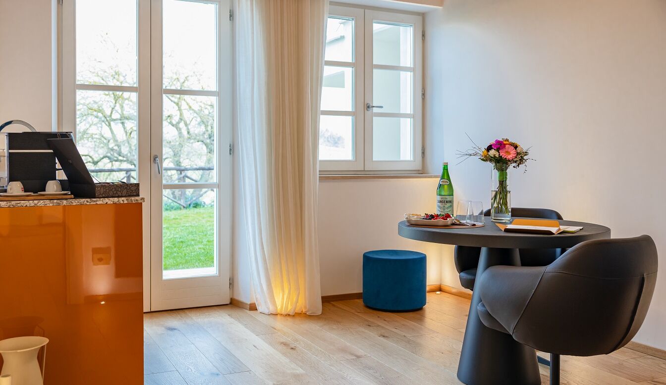 A modern room with a dining table, a chair, a coffee machine, and a window with curtains.