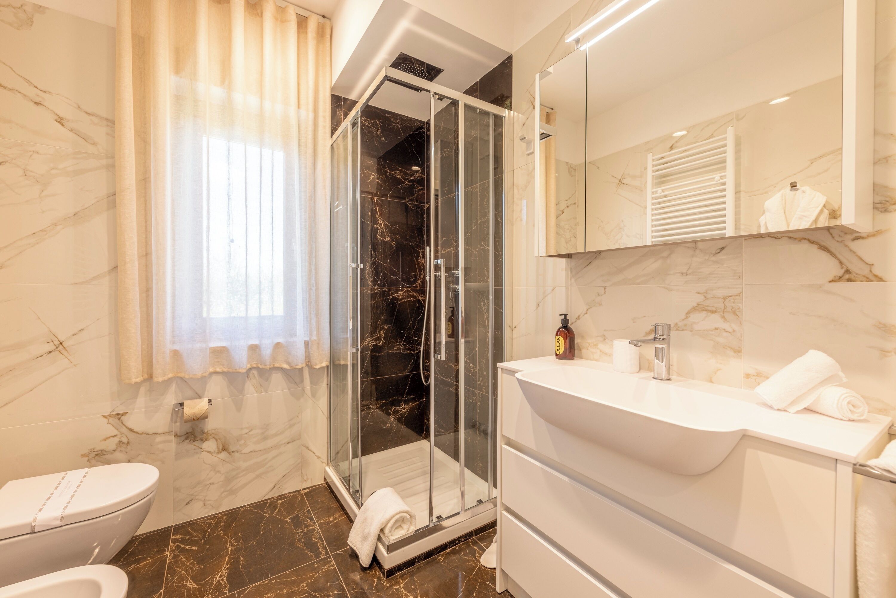 Ein modernes Badezimmer mit einer gläsernen Duschkabine, einem weißen Waschbecken und einem marmorbodenbelagten Boden.