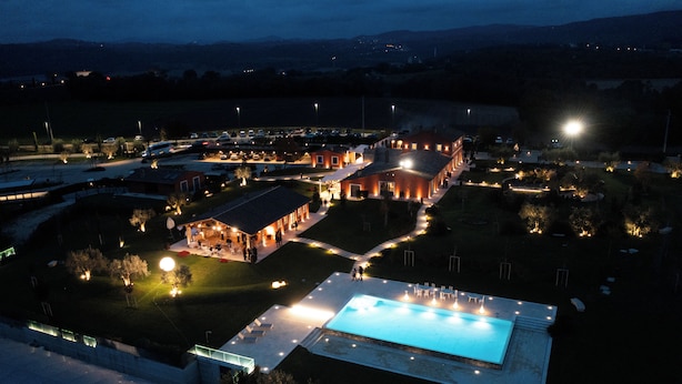 Vista aérea de un resort con piscina, varias construcciones e iluminación exterior.