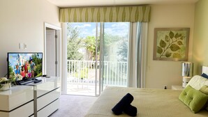 Un dormitorio con cama, televisión, escritorio y balcón.