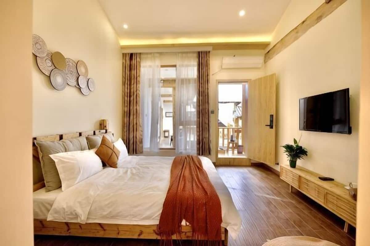 A bedroom with a large bed, a TV, a plant, and a view of the outdoors.