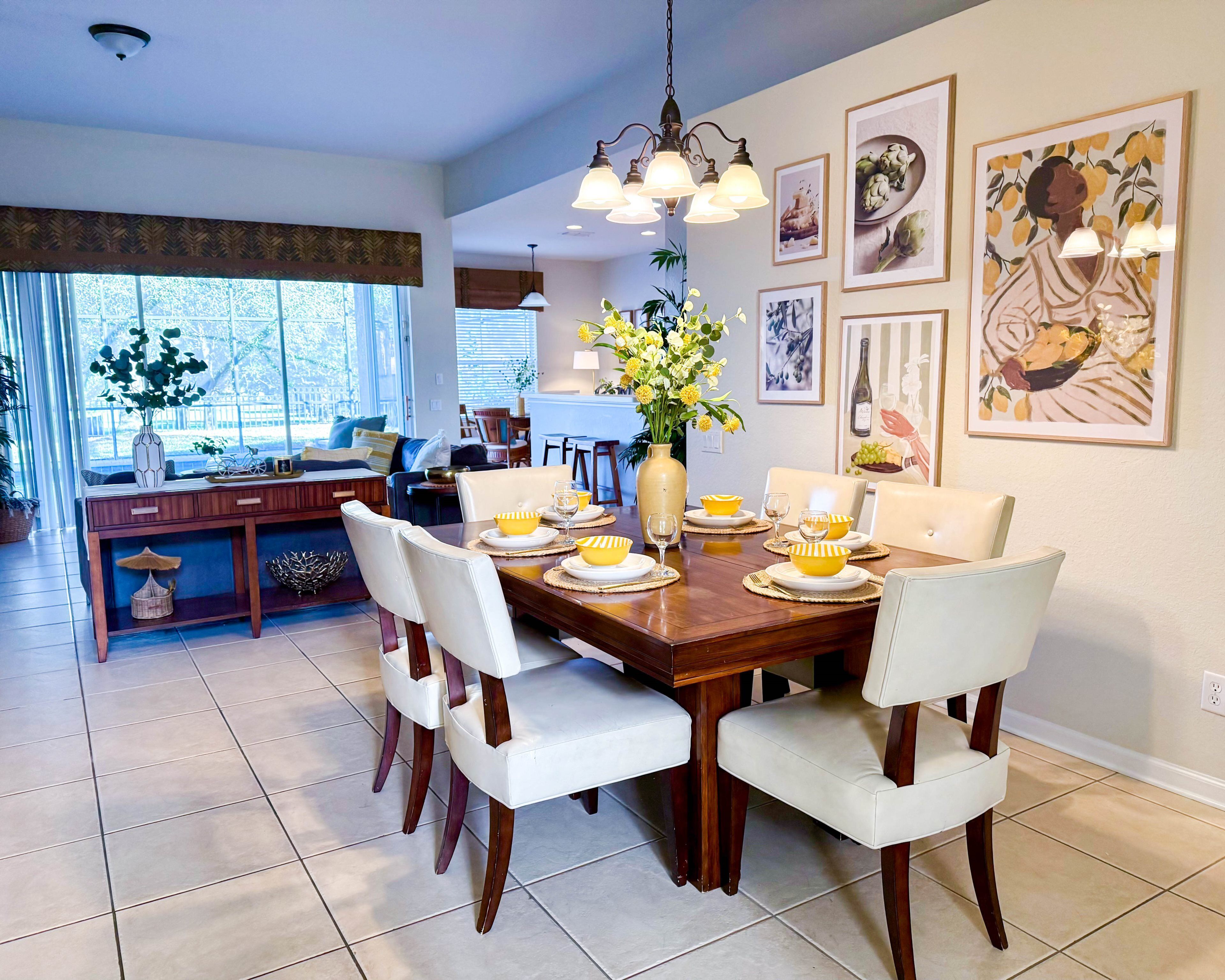 A dining area with a wooden table set for four, white chairs, and a vase of flowers.