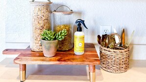 Una encimera de cocina con armarios de madera, un florero de vidrio con suculentas, un pulverizador metálico y una cesta tejida con utensilios.