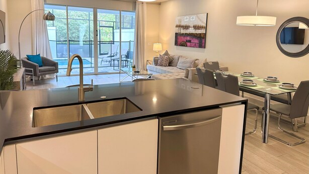 A modern kitchen with a central island, dining area with chairs and a table, and a seating area with a sofa and chairs.