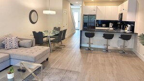 A modern kitchen with a central island, bar stools, and a dining area with a sofa and coffee table.