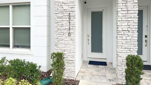 A modern building with a stone facade, a white door, and a small porch area with plants.