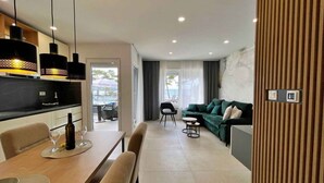 A modern living room with a sofa, a dining table with chairs, and a kitchen area with a countertop and hanging lights. - Holiday apartment with swimming pool and sea view (Šilo)