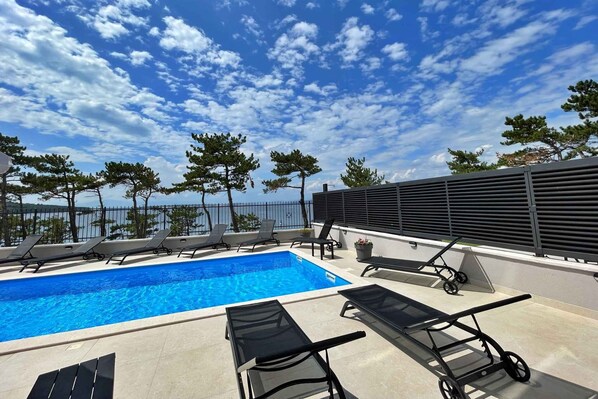 A rooftop pool area with lounge chairs and a view of the sea.