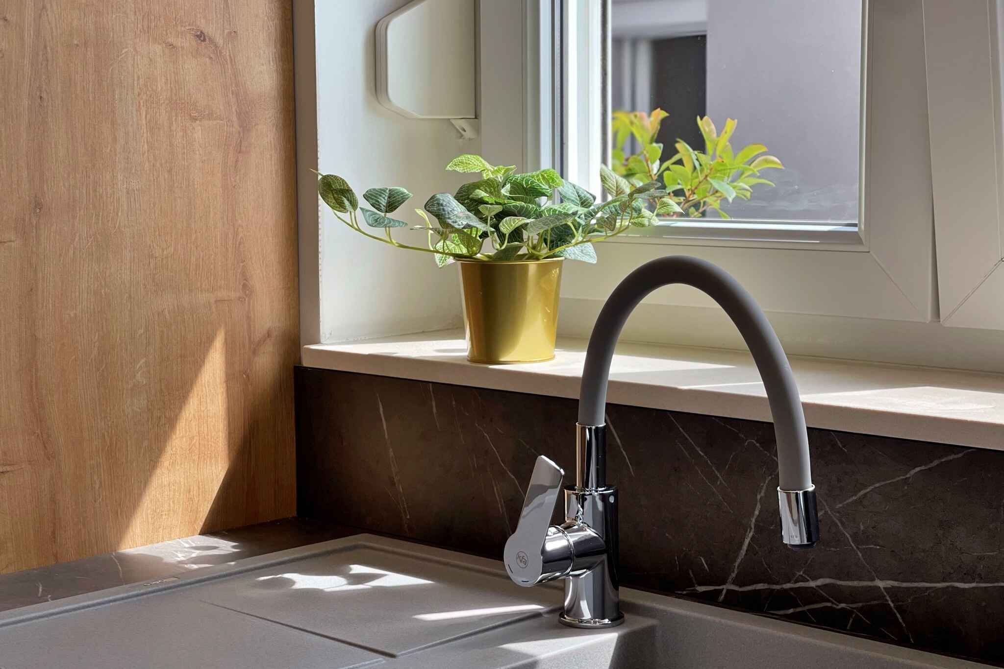 A bathroom with a modern faucet, a potted plant, and a window providing natural light.