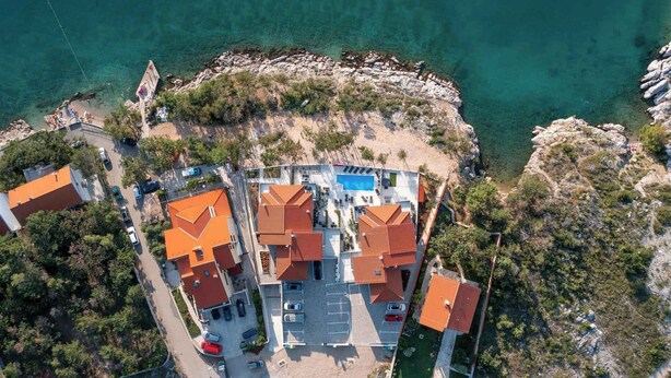 An aerial view of a coastal hotel with multiple buildings, a swimming pool, and a parking area. - Holiday apartment with swimming pool and sea view (Šilo)
