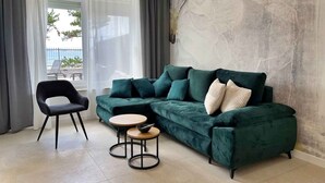 A modern living room with a green sectional sofa, a black armchair, and two round tables. - Holiday apartment with swimming pool and sea view (Šilo)