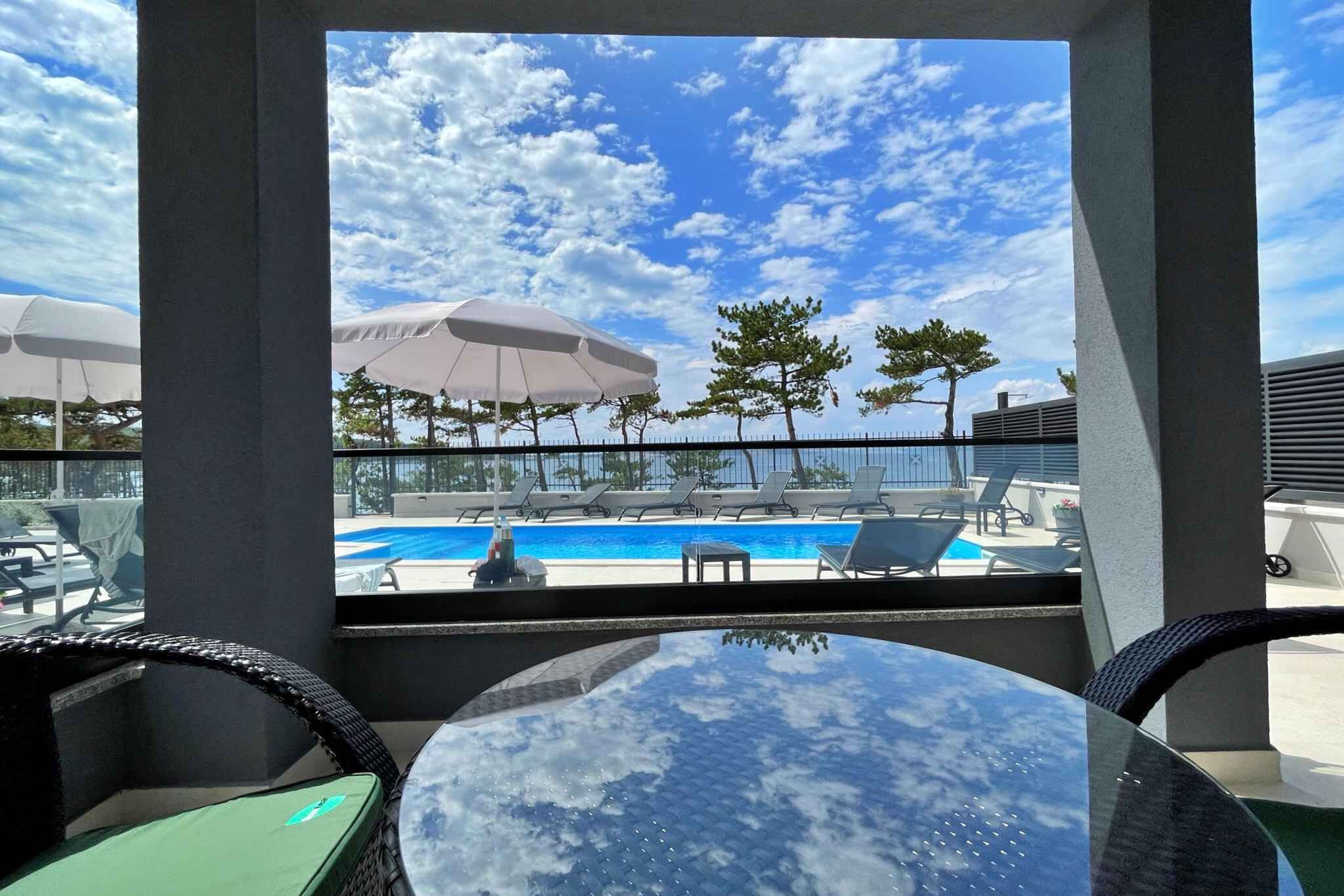 Et tag med swimmingpool, liggestole og parasoller, en klar himmel og udsigt over poolen.