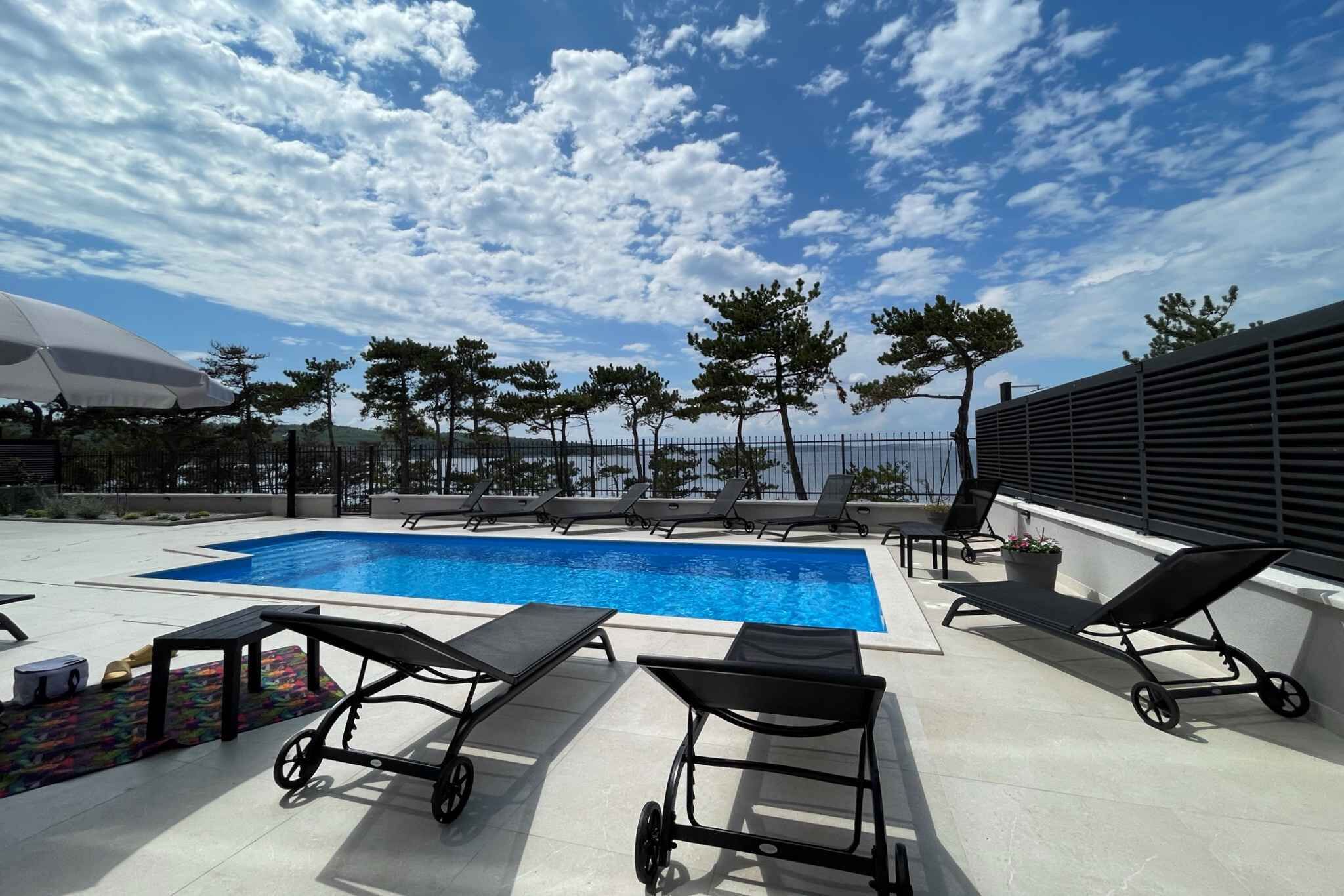 Area piscina sul tetto con poltrone relax, un tavolino e una pianta in vaso.