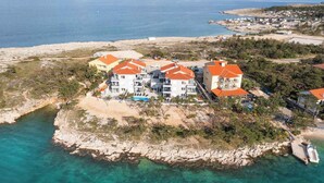 A coastal property with multiple buildings featuring red roofs, situated on a rocky island with clear blue waters. - Holiday apartment with swimming pool and sea view (Šilo)