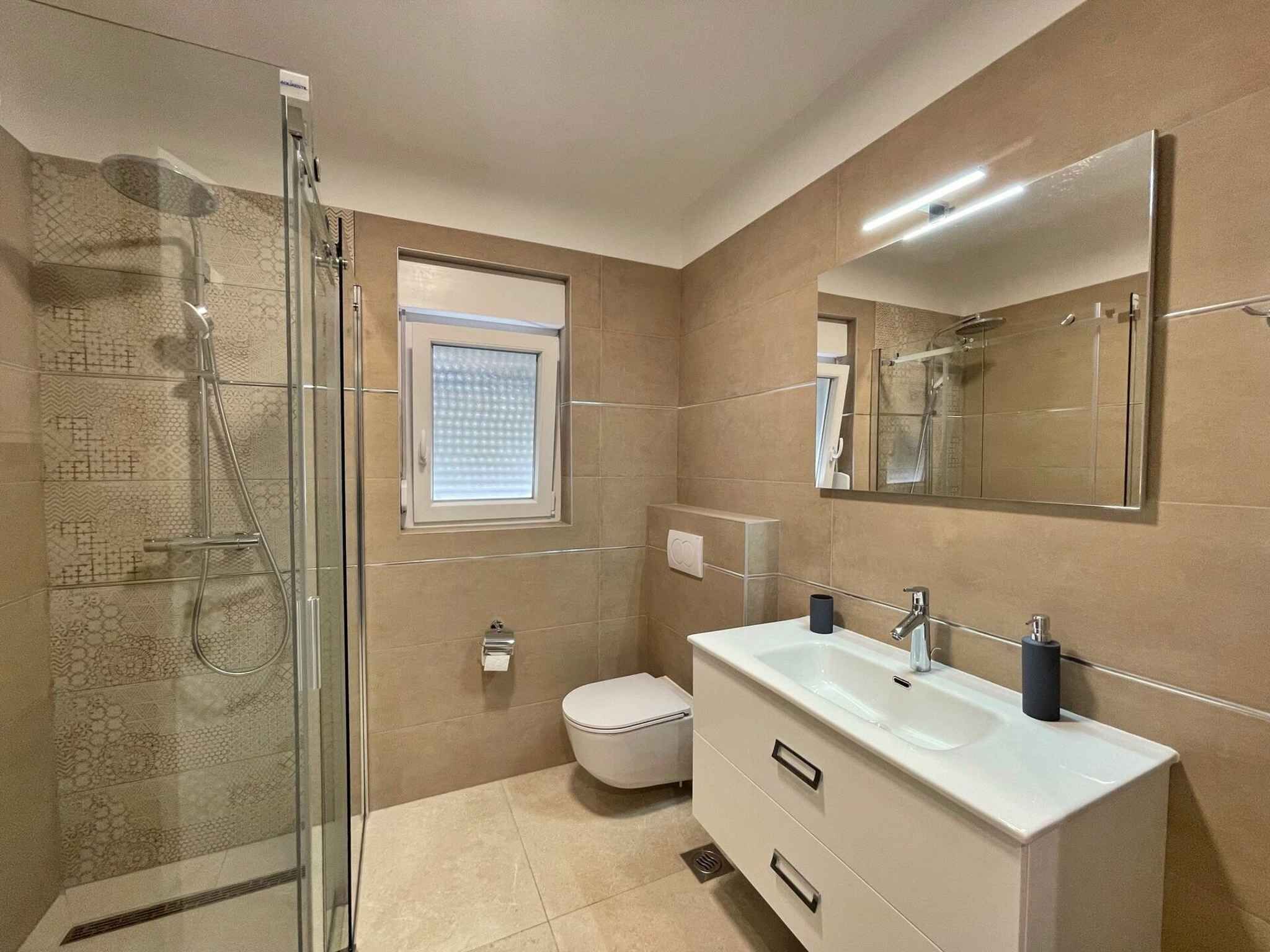 A modern bathroom with a glass shower enclosure, a toilet, a sink with a mirror, and a window.