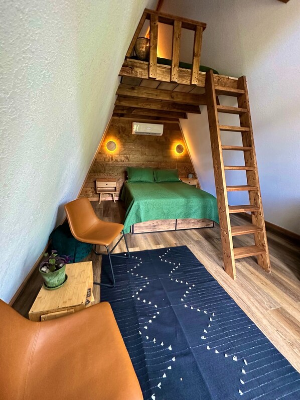 A loft bedroom with a wooden ladder, a green bed, a desk, and a chair.