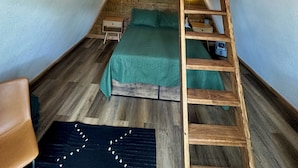 Camera mansarda in stile loft con una scala in legno, letti a castello e un lampadario.