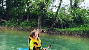 Una persona su un kayak che naviga in un fiume circondato da alberi.