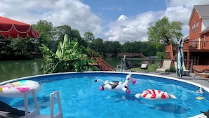 A swimming pool with inflatable toys, a wooden deck, and a view of a lake and buildings in the background. - The Dream Lakehouse  (Florence)