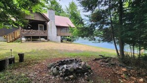 A cabin with a stone fire pit, a deck, and a view of a lake.