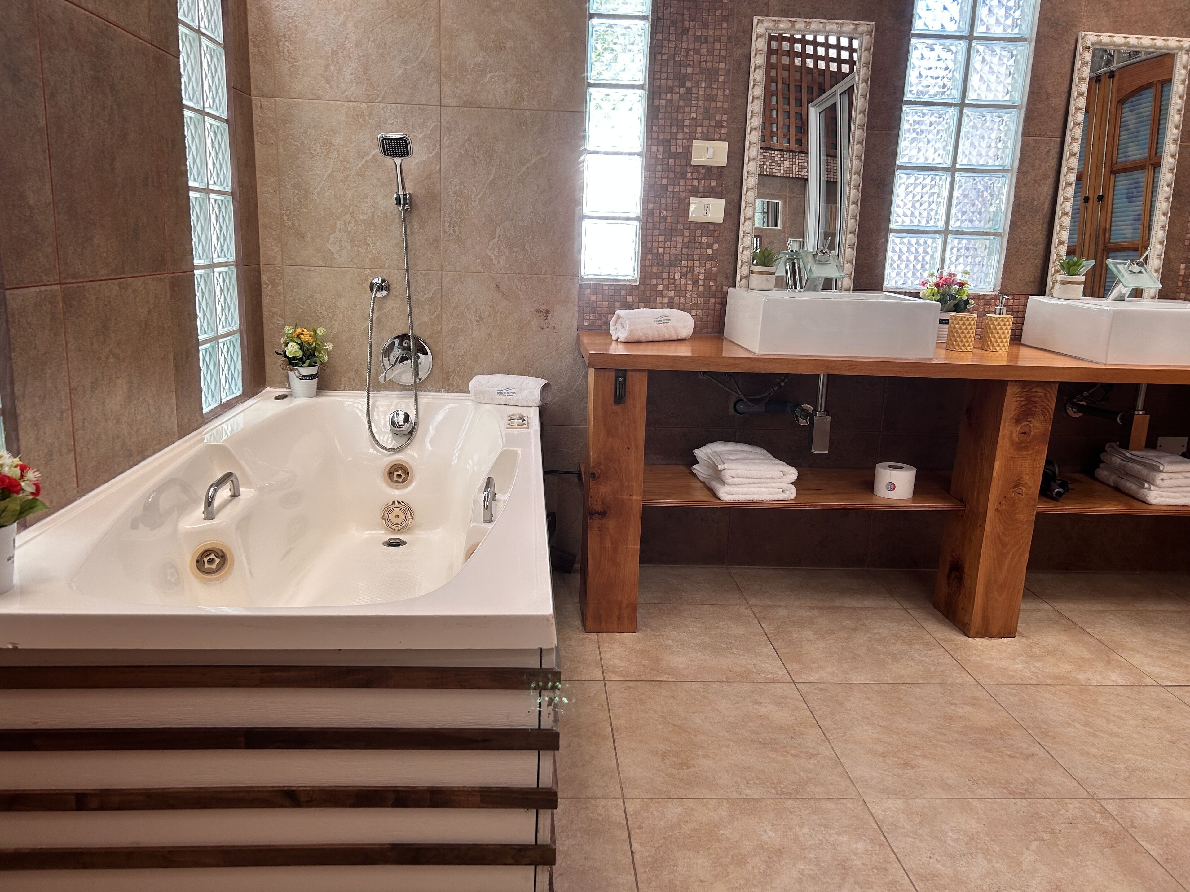 A modern bathroom with a large bathtub, a wooden vanity with two sinks, and a mirror.