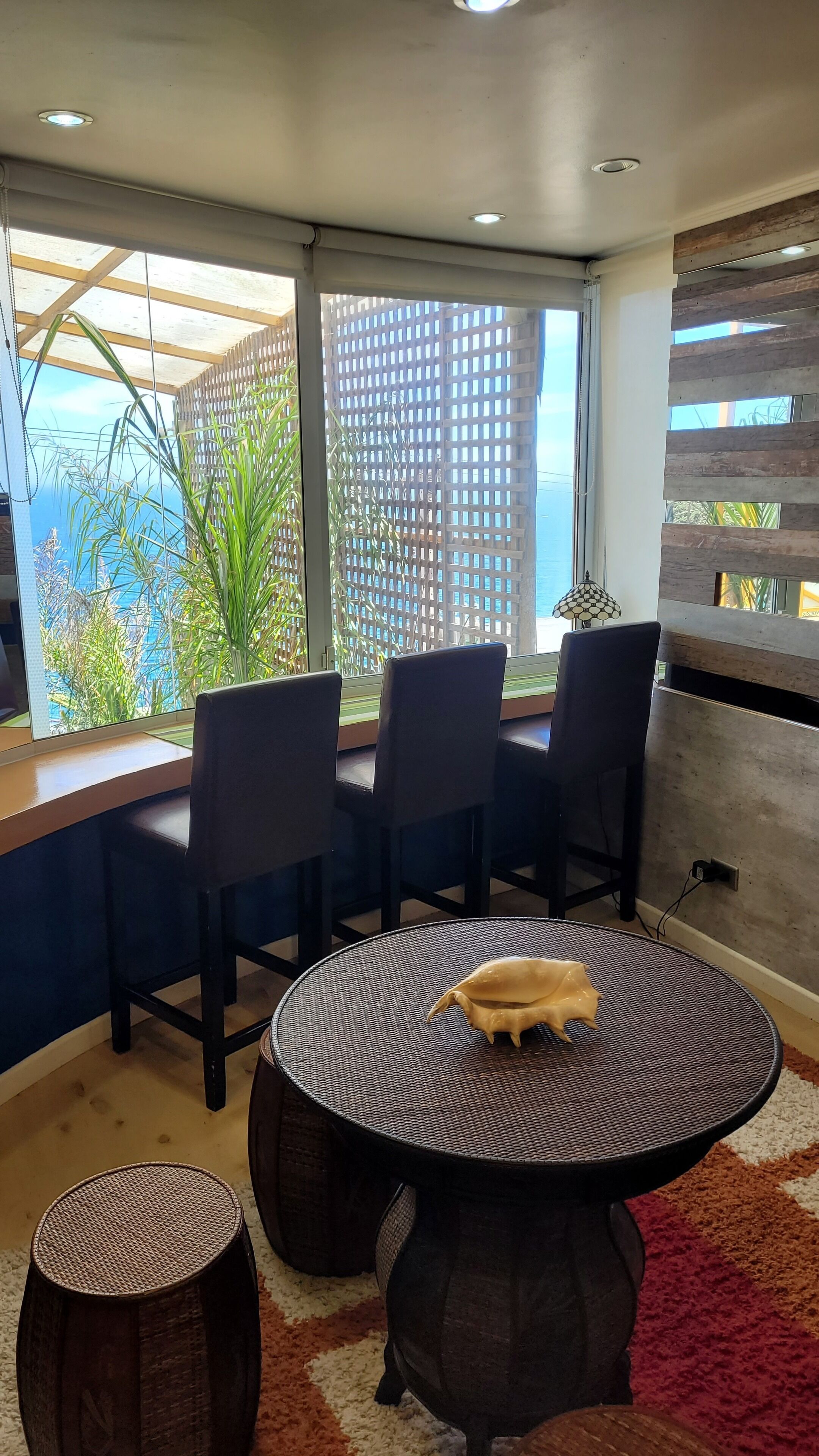 Un comedor moderno con una mesa redonda, cuatro sillas y vistas a un paisaje urbano a través de amplios ventanales.