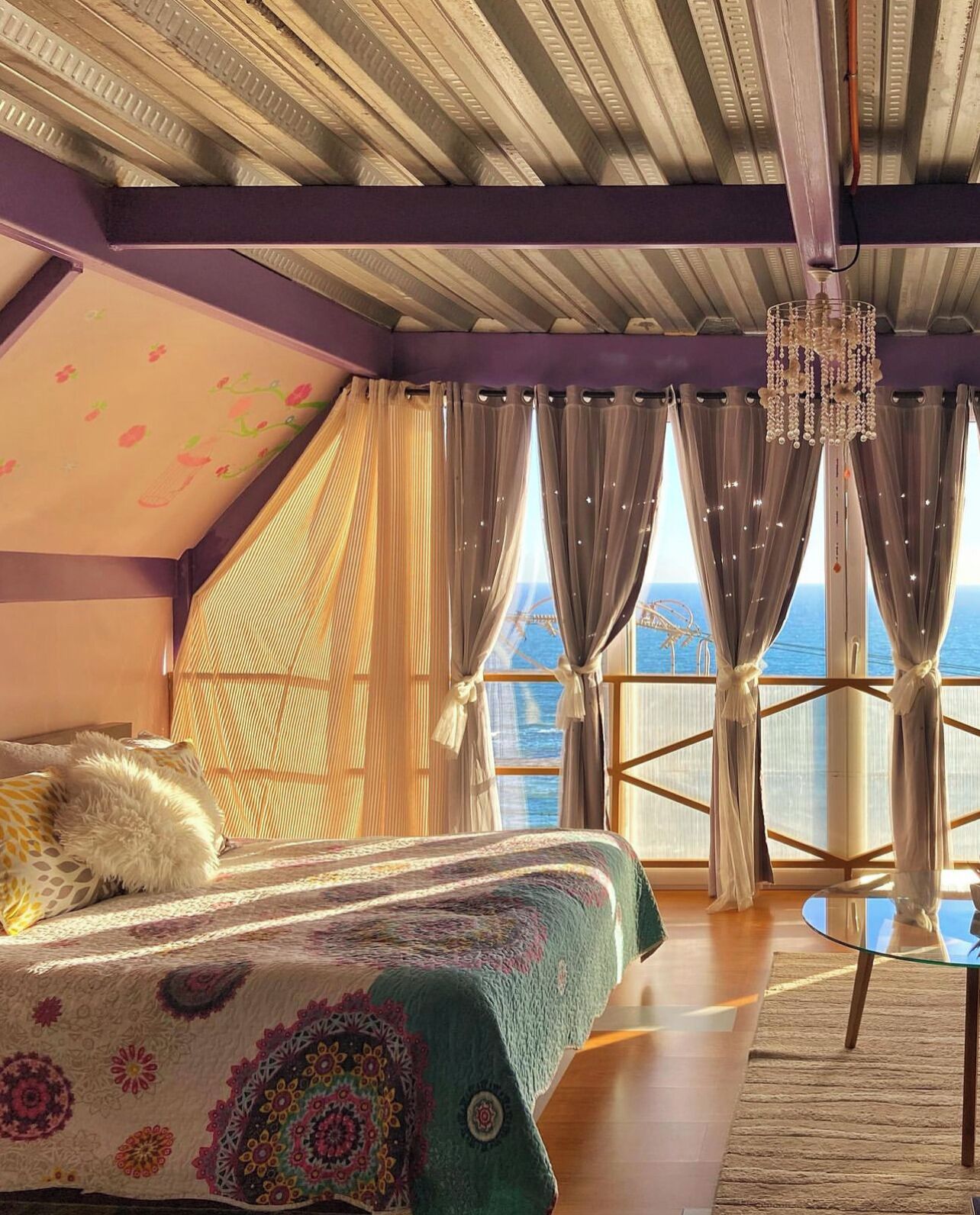 Een slaapkamer met een groot bed, uitzicht op zee en een balkon met gordijnen.