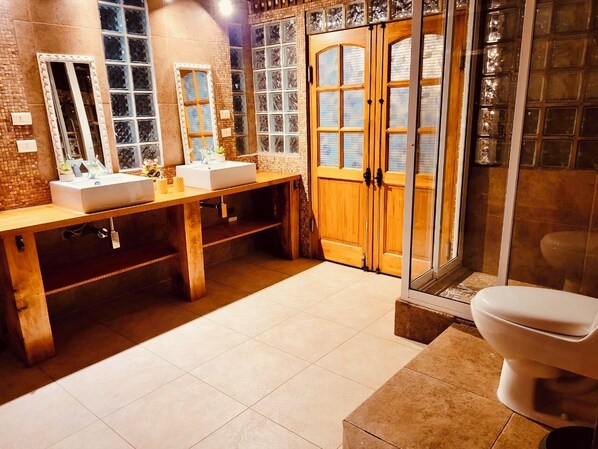 A bathroom with three sinks, a wooden vanity, a glass shower enclosure, and a white toilet.