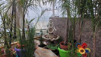 Ein Garten mit einer Statue eines Kindes, das eine Schale hält, umgeben von verschiedenen Blumentöpfen und einem gepflasterten Weg.