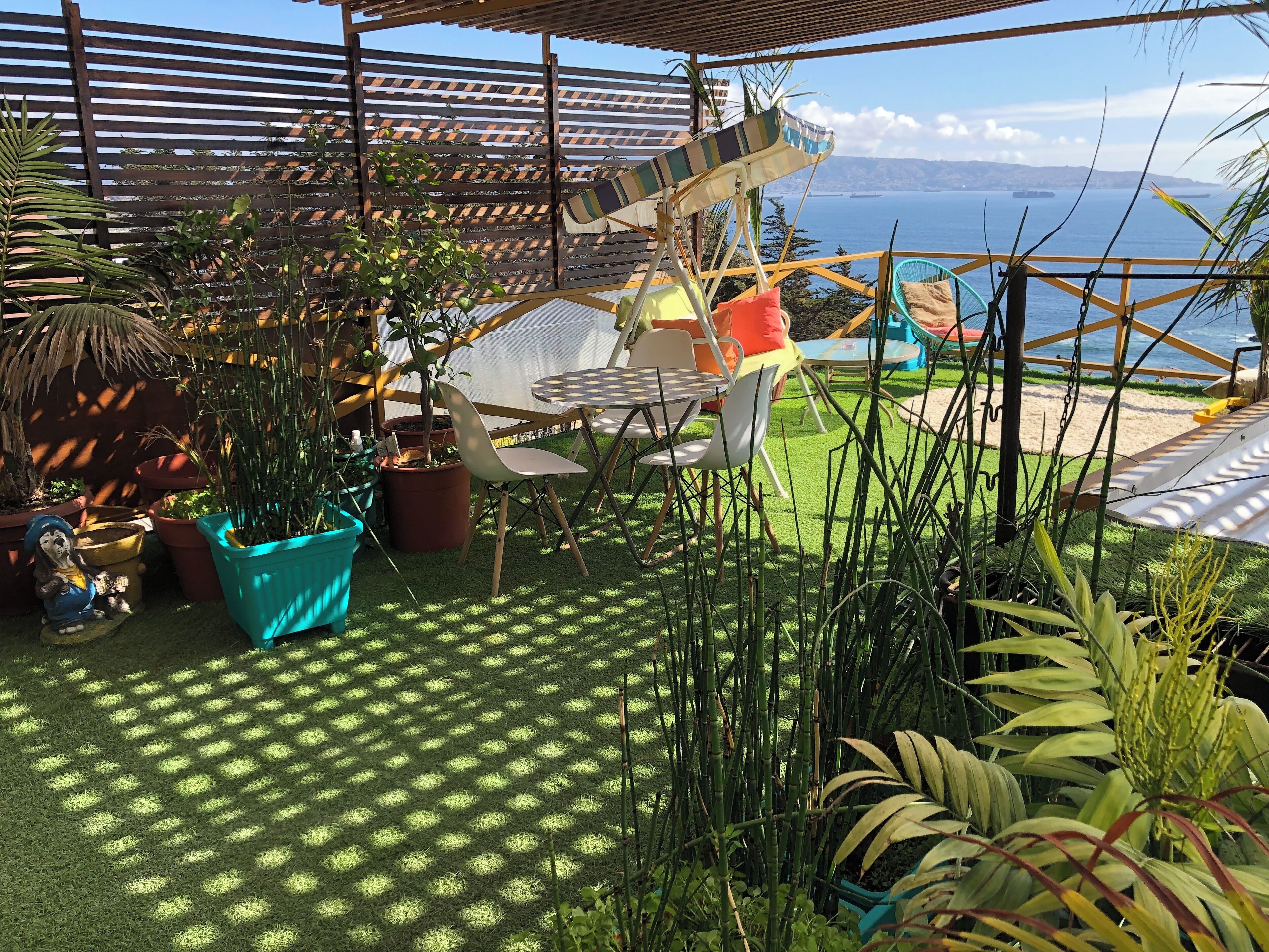 Un patio con vista al mar, con una mesa, sillas y plantas en macetas.