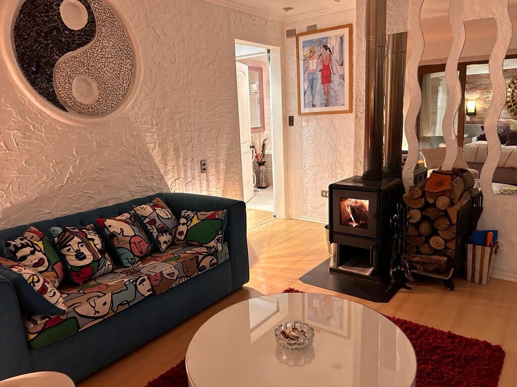 Una sala de estar con un sofá azul, una mesa de centro redonda de vidrio, un estufa de leña y un gran símbolo del yin y el yang en la pared.