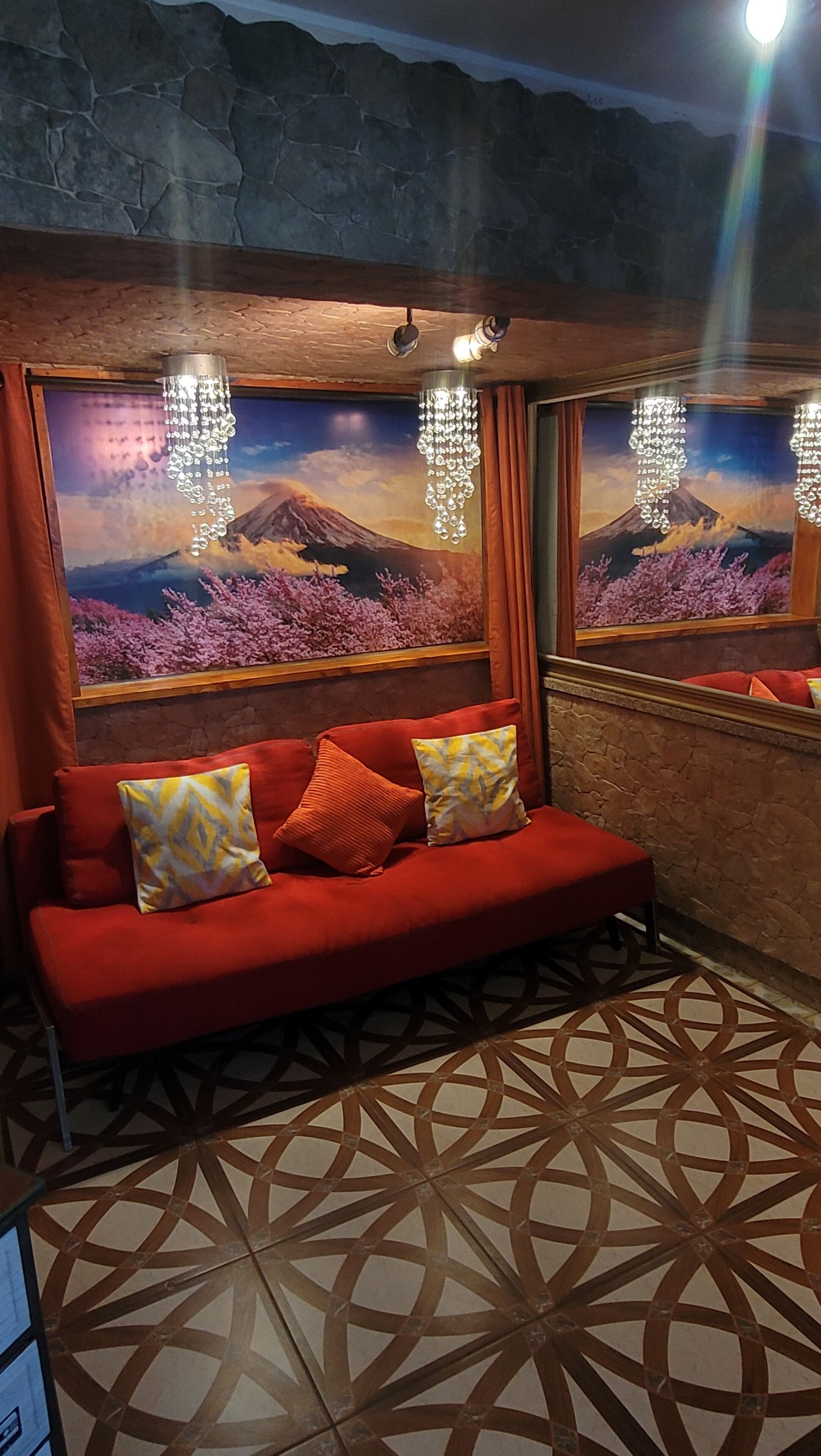 A red sofa with patterned cushions, a decorative mirror, and a view of a mountain landscape through a window.