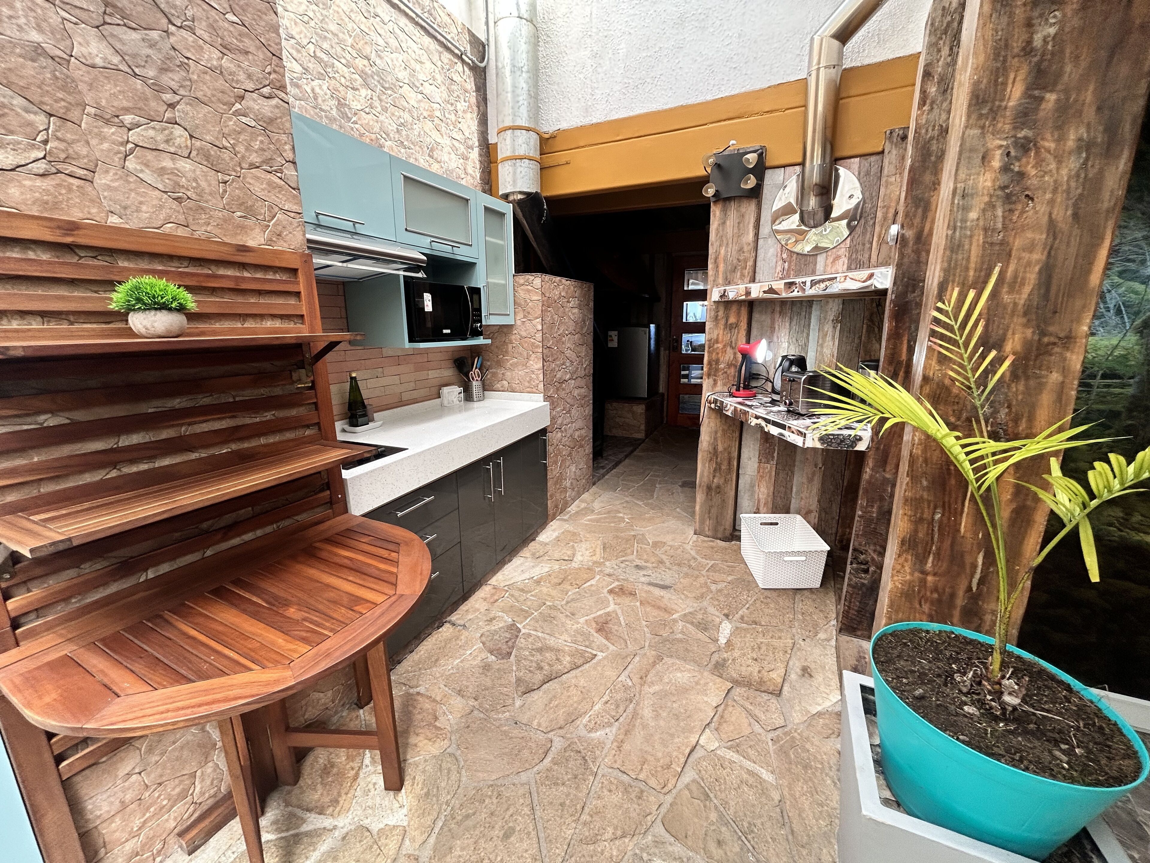 A compact kitchen with a stone backsplash, wooden shelves, and a small dining table.