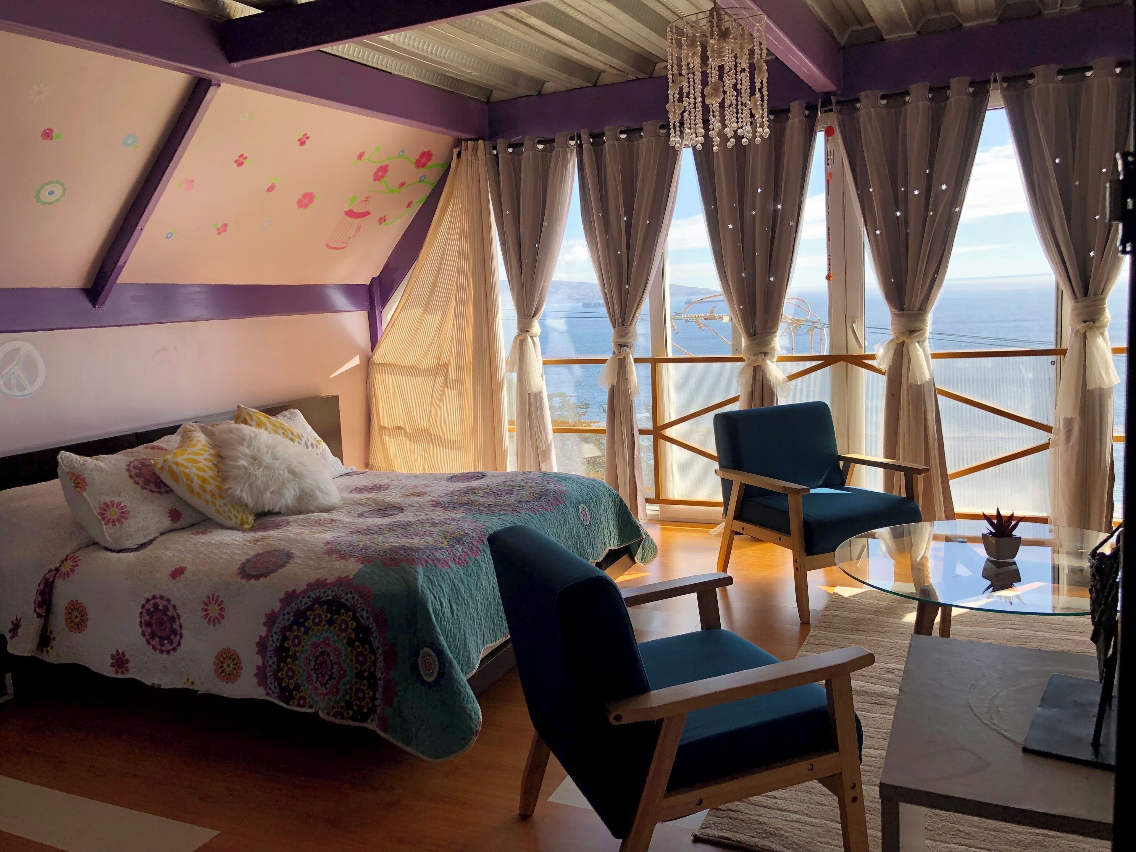 Une chambre à coucher avec un lit, une chaise, une table et de grandes fenêtres avec des rideaux.