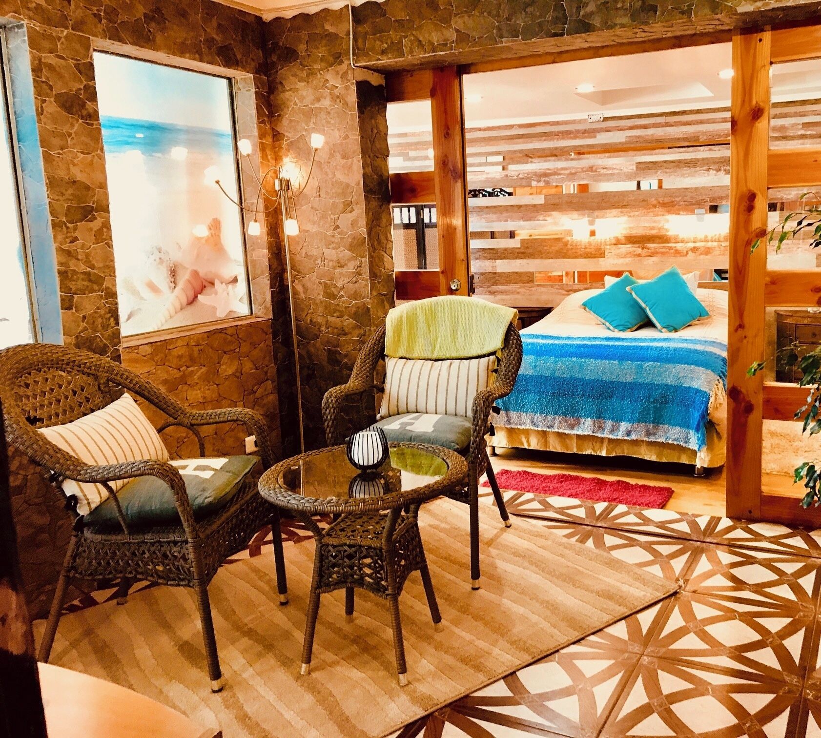 A cozy room with wicker furniture, a bed with blue bedding, and a large window with a view.